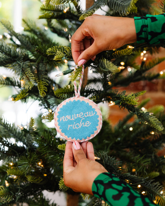 Person hanging a Christmas ornament on a tree with blurred lights in the background