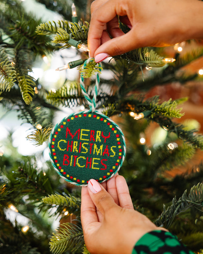 Person holding a 'Merry Christmas Bitches' ornament on a decorated tree