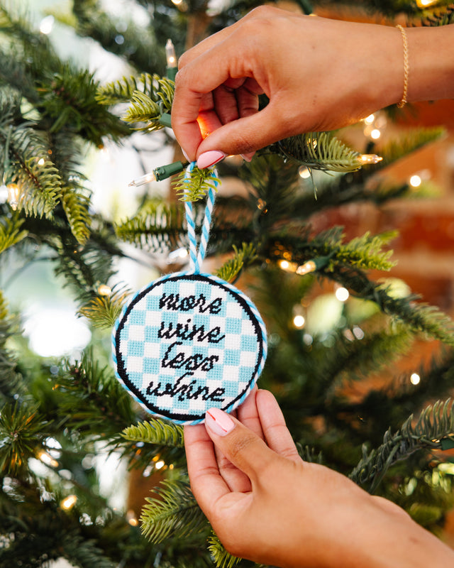 Hand holding a decorative ornament with text against a Christmas tree background