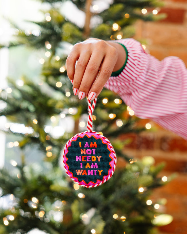 Person holding a colorful ornament with text in front of a Christmas tree