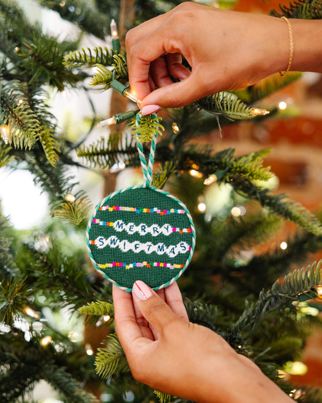 Hand holding a festive ornament with 'Merry Swiffermas' text on a decorated Christmas tree.