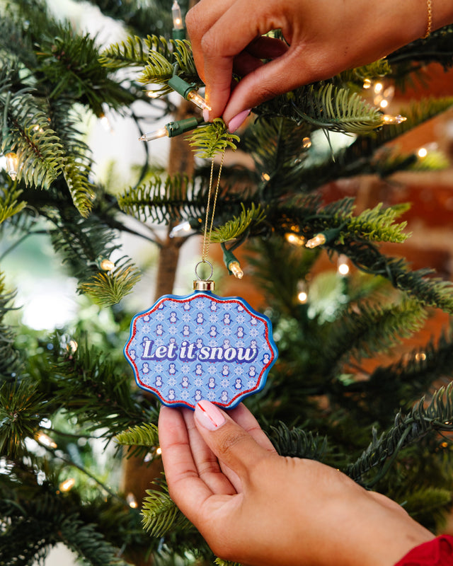 Person decorating a Christmas tree with a 'Let it snow' ornament.