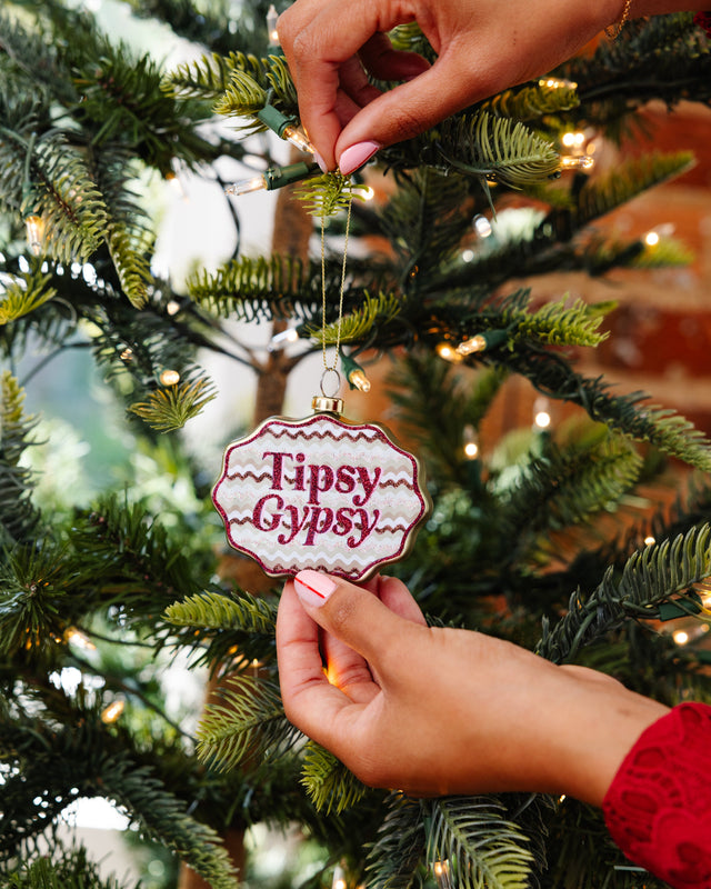 Hand holding a 'Tipsy Gypsy' ornament on a Christmas tree.