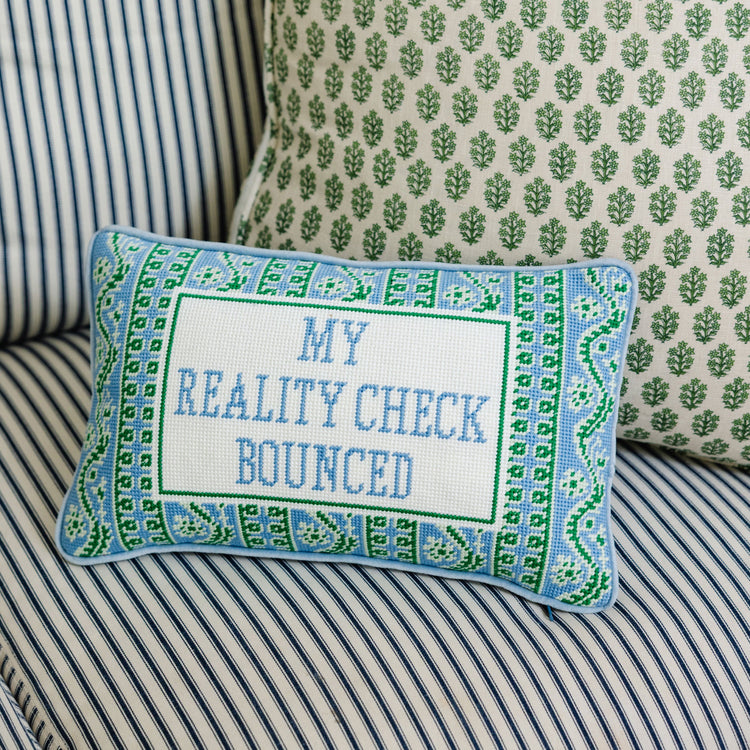 Decorative pillow with text 'My Reality Check Bounced' on a striped sofa.