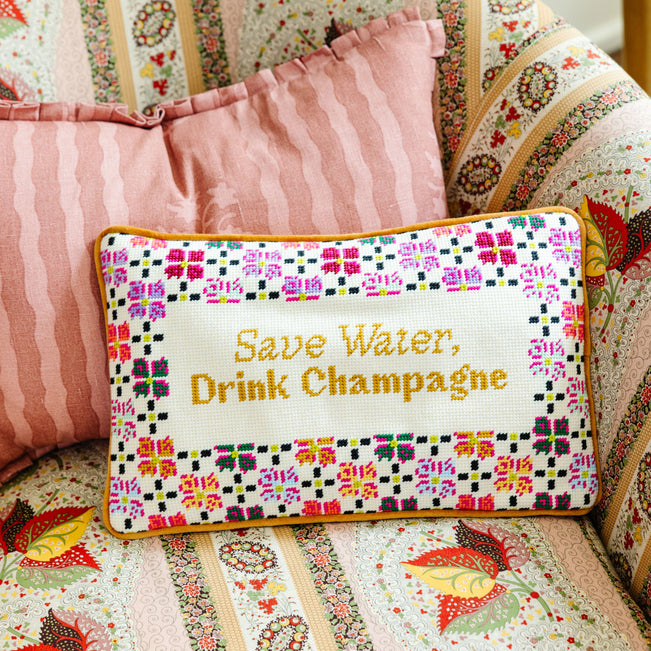 Decorative pillow with 'Save Water, Drink Champagne' text on a patterned couch.
