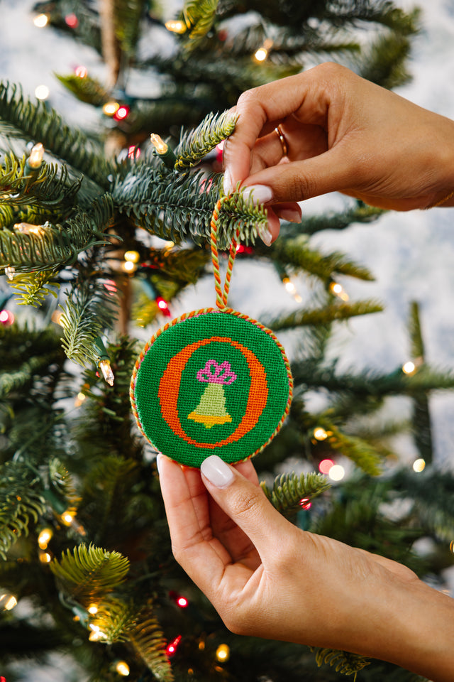 Hand holding a decorative ornament with a Christmas tree in the background
