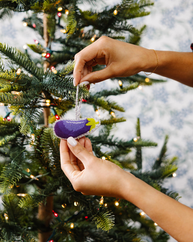 Two hands holding a small ornament near a decorated Christmas tree.