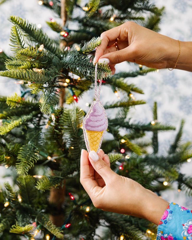 Hand holding a colorful ice cream cone ornament against a Christmas tree background