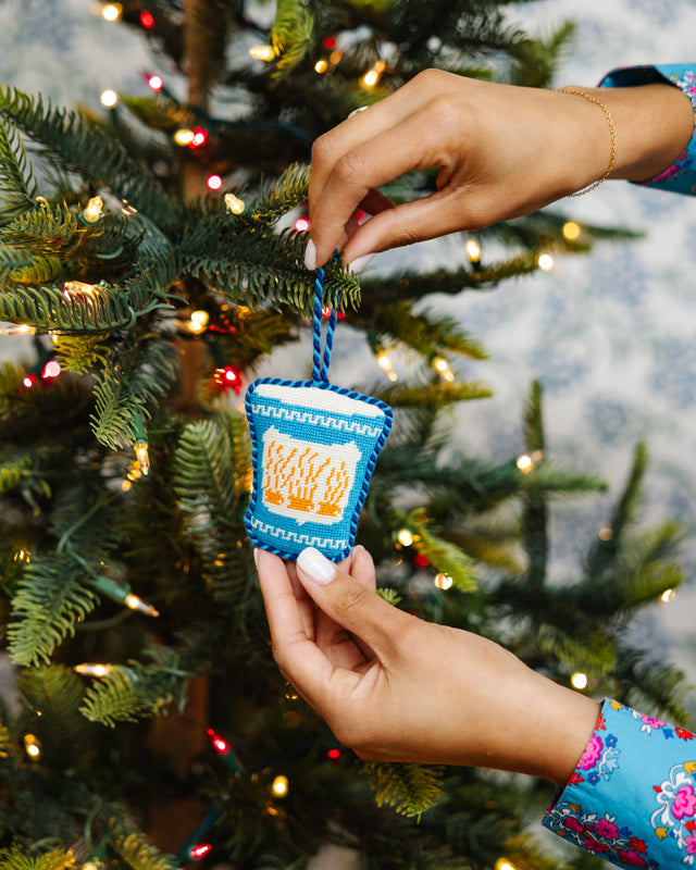 Person holding a small blue ornament with text against a decorated Christmas tree.