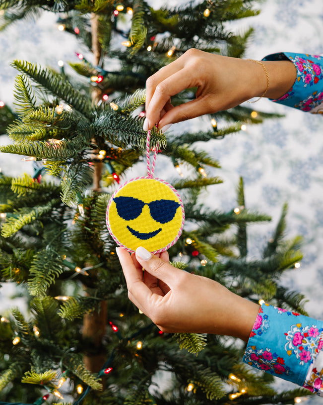 Person decorating a Christmas tree with a smiley face ornament wearing sunglasses.