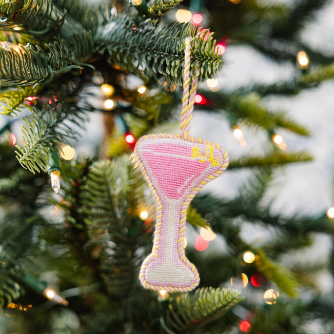 Decorative martini glass ornament on a Christmas tree with lights in the background