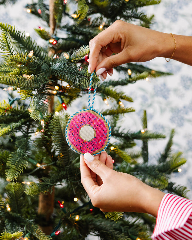 Person decorating a Christmas tree with a pink ornament.