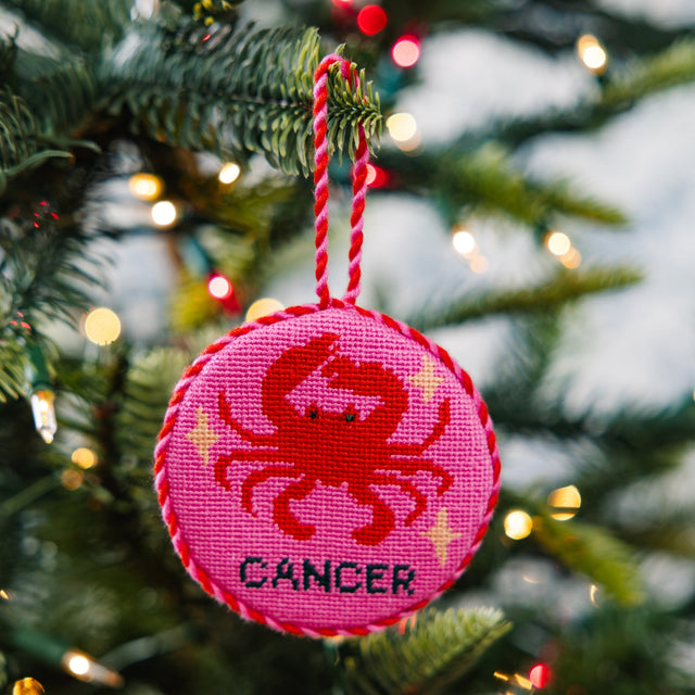 Decorative ornament with a red crab design and 'Cancer' text on a pink background, hanging on a Christmas tree.