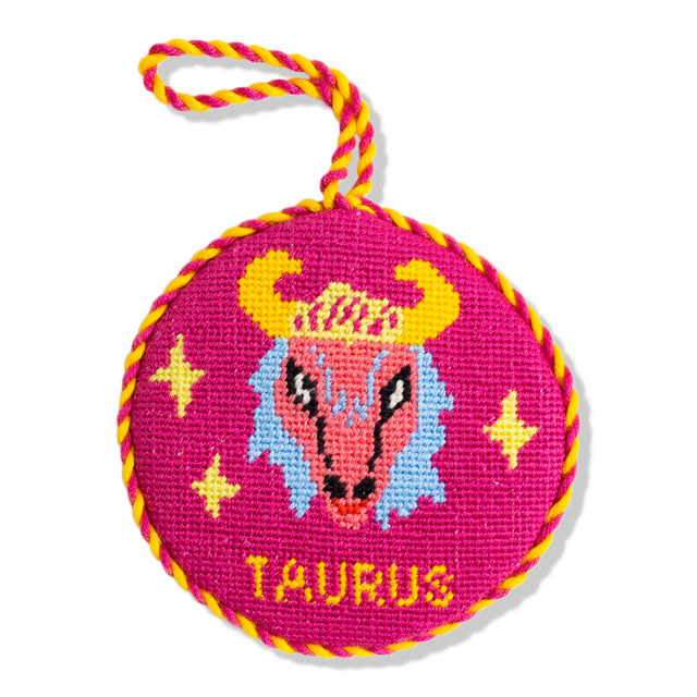 Circular pink needlepoint with Taurus design and yellow rope handle on a white background