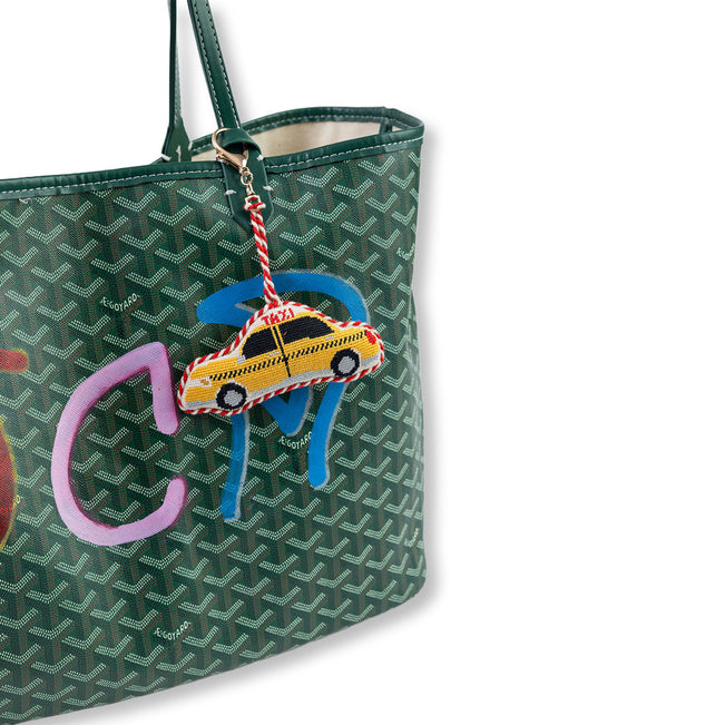 Green patterned handbag with a colorful charm featuring a taxi and pink elephant on a white background