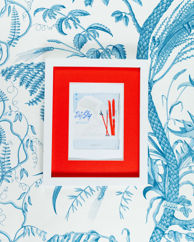 Big Sky Matchbook - Furbish Studio, A Big Sky Montana watercolor print featuring ski poles and snowblades painted in red with a bluish background color and an iceberg in  a 5x7 white frame with a wallpaper background