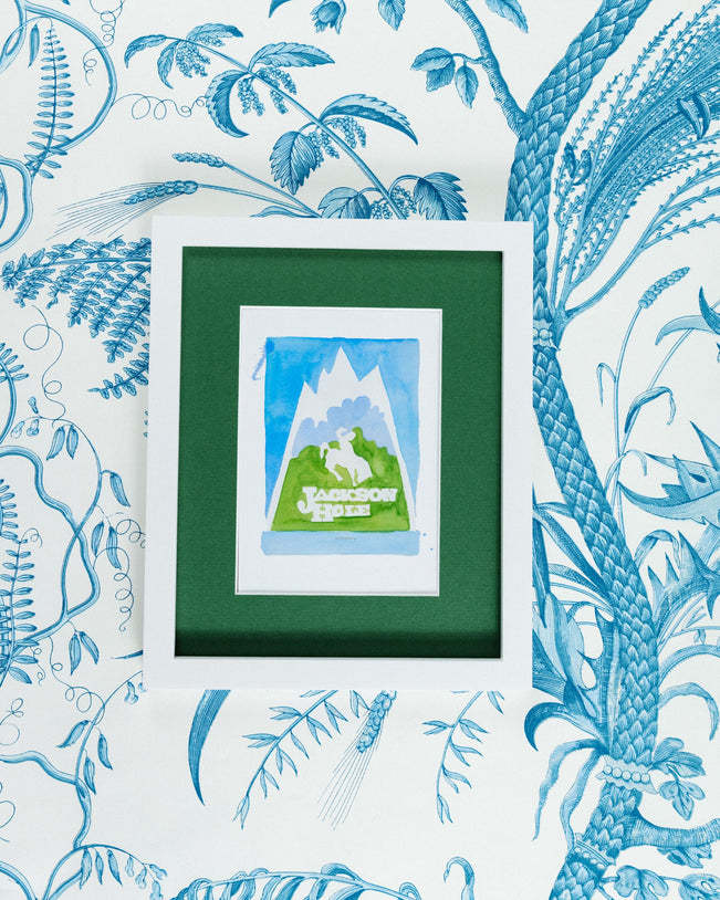 Jackson Hole Matchbook - Furbish Studio, Jackson Hole matchbook watercolor print illustrating the town's scenery painted in light blue and mud green in a 5x7 white frame with a wallpaper background